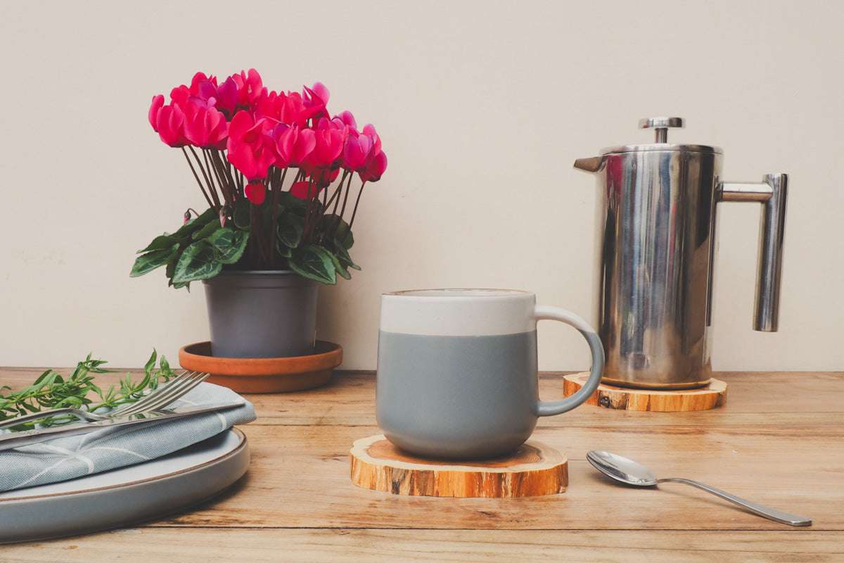 Scandi style mug resting on a handcrafted wooden yew coaster with flowers and a cafetière also on a yew coaster 