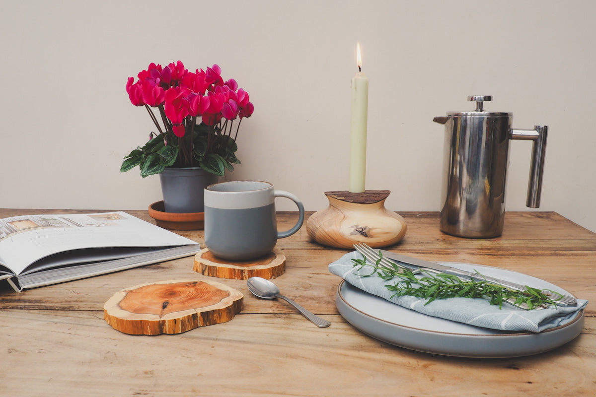 A decorated table with plates, book, candle with flame in wooden candle holder and a mug on a wooden yew coaster