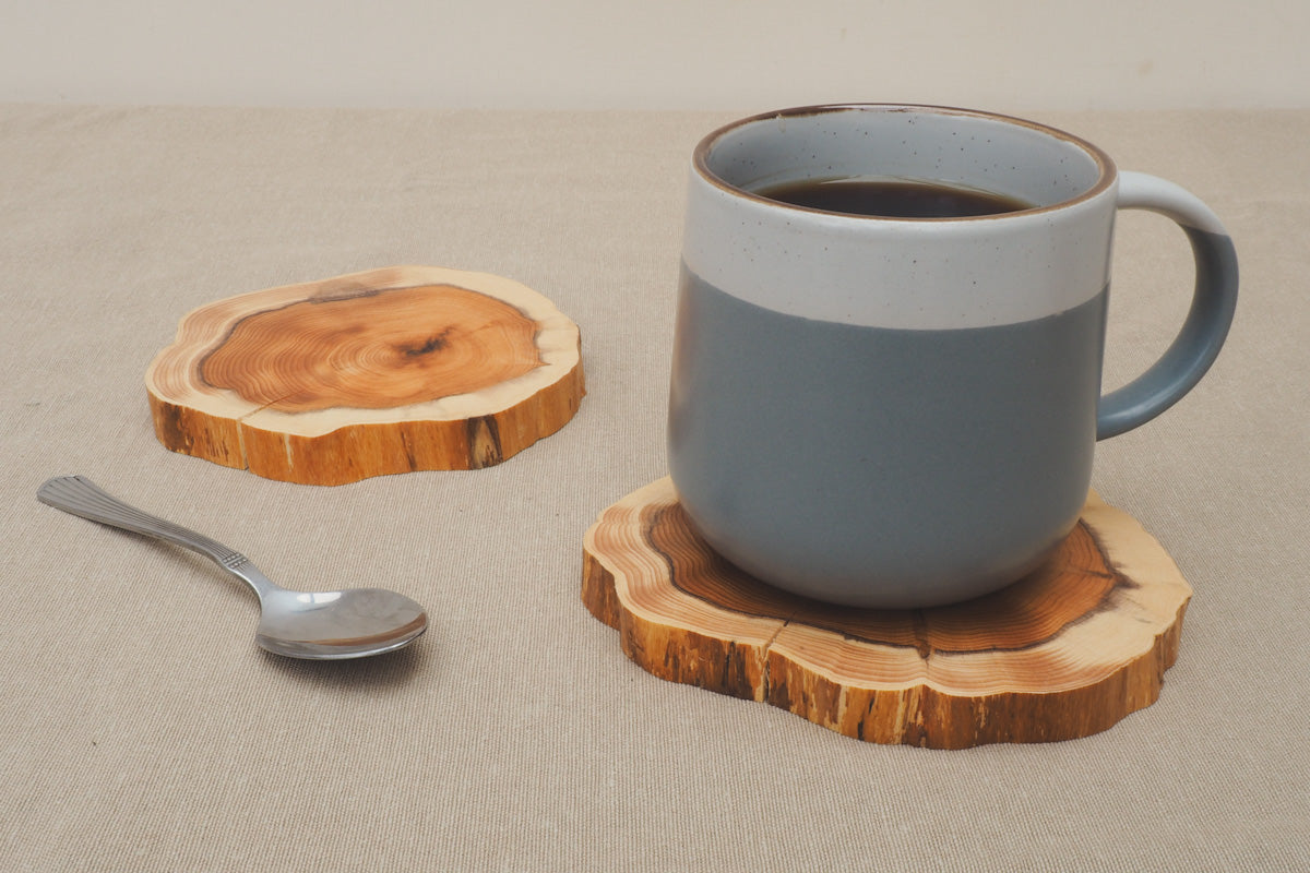 Close up shot of a mug of coffee and two wooden handcrafted yew coasters with a teaspoon 