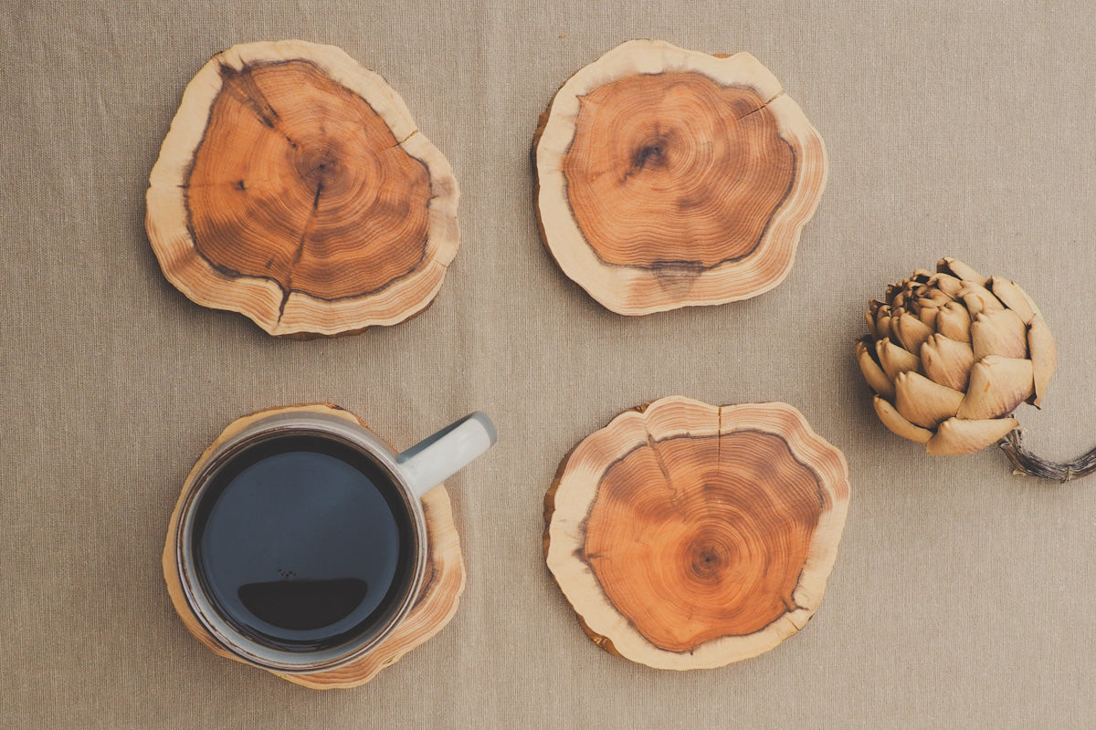 looking down on 4 wooden yew coasters, one of which has a mug of coffee on it