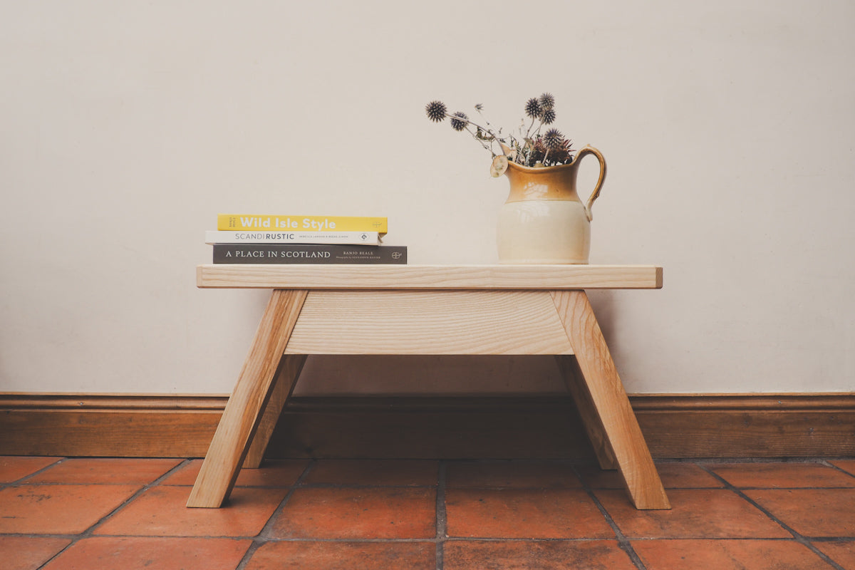 A stool is being used as a coffee table with books and a house plant on it.