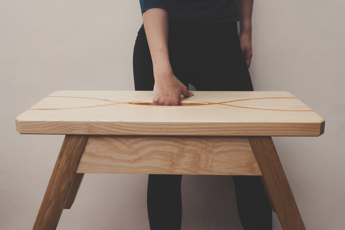 A person is using the hand hole in the top of the stool to lift it up