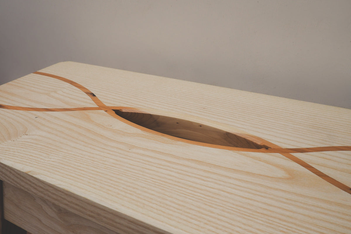 A close up of the grain on the top of the stool. There is two contrasting yew stripes runnning over it in a criss-cross pattern